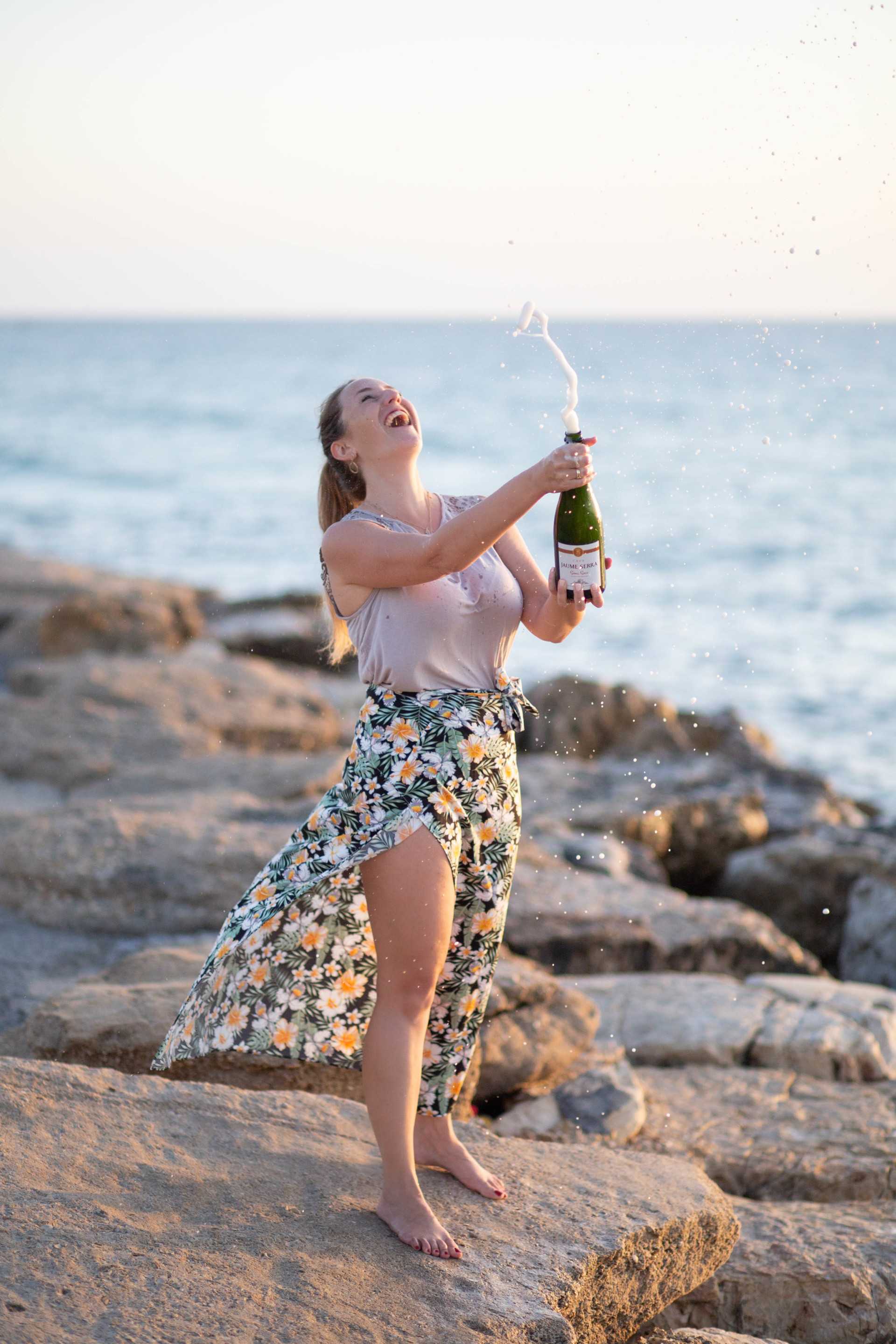 אני עומדת על סלעים בחוף הים עם בקבוק יין